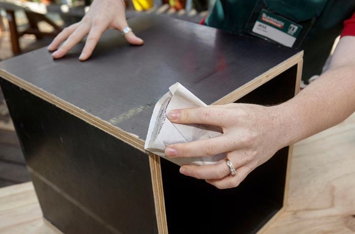 A constructed wooden storage box being sanded down with sandpaper