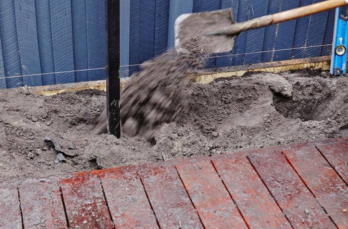 A person backfilling a post hole with soil