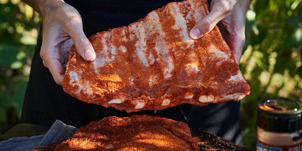 A person holding some ribs that have been seasoned with a rub.