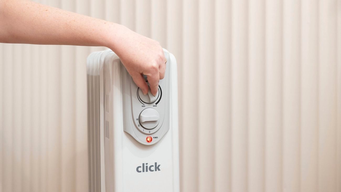 A person is adjusting the temperature on an oil heater.