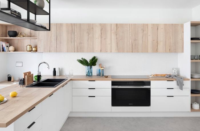 Modern white kitchen with timber benchtop and cabinets, suspended shelving and concrete floor
