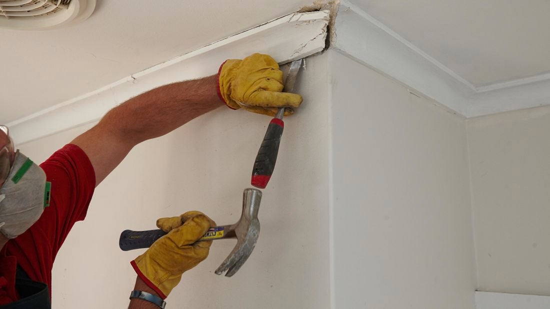 A person removing cornice with a hammer and chisel