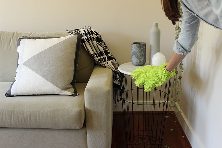 Person cleaning a side table using a dusting glove 