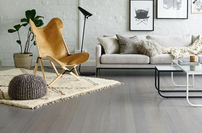 Room with wooden flooring along with a couch, black and white tables, rug, chair, plant and light. 