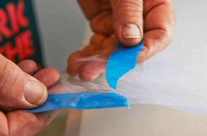 A person using masking tape to peel the backing off a sheet of frosting
