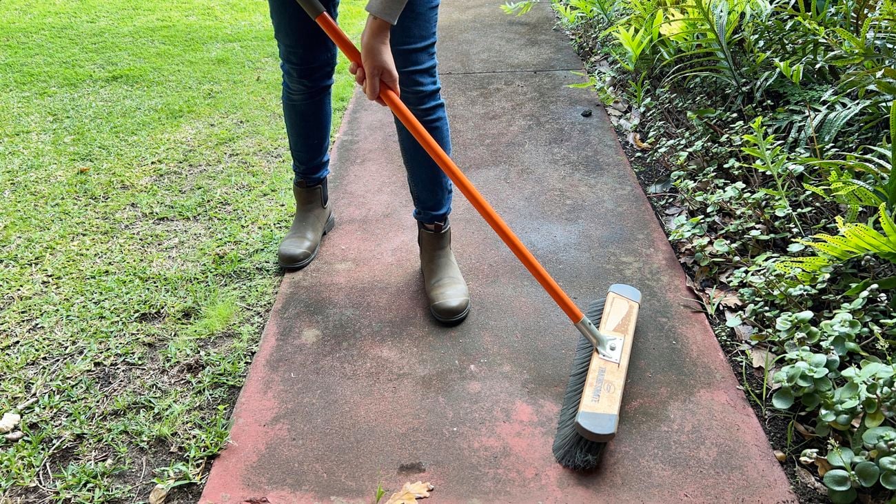 Person using broom to sweep concrete.
