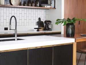 Modern kitchen with a white benchtop with crockery on it, black and white splashback with a shelf attached to it and a wooden table next to it.