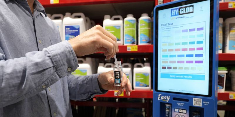 Customer testing pool water using a test strip beside a Hy-Clor digital water testing station in a Bunnings store.