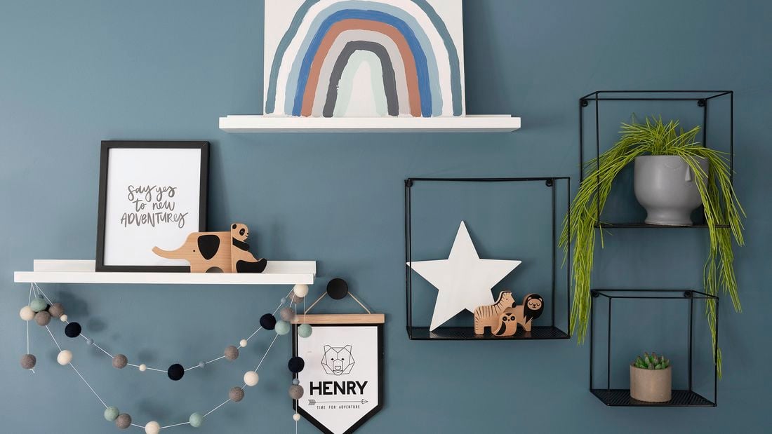 Blue wall with wall shelves that have various decorative items on them like paintings and plants.