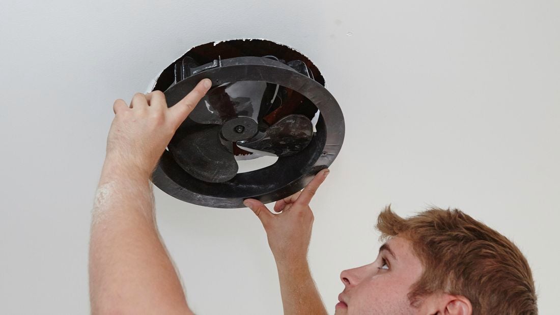 A person inserting an exhaust fan into a hole in a ceiling