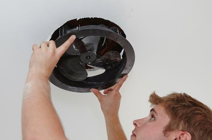A person inserting an exhaust fan into a hole in a ceiling