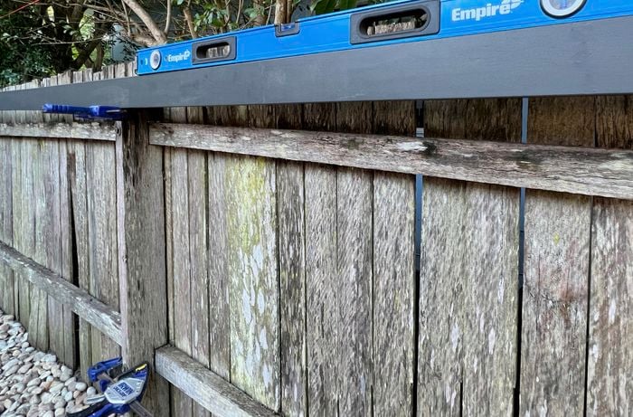 Line level sitting on top of an unpainted wooden fence