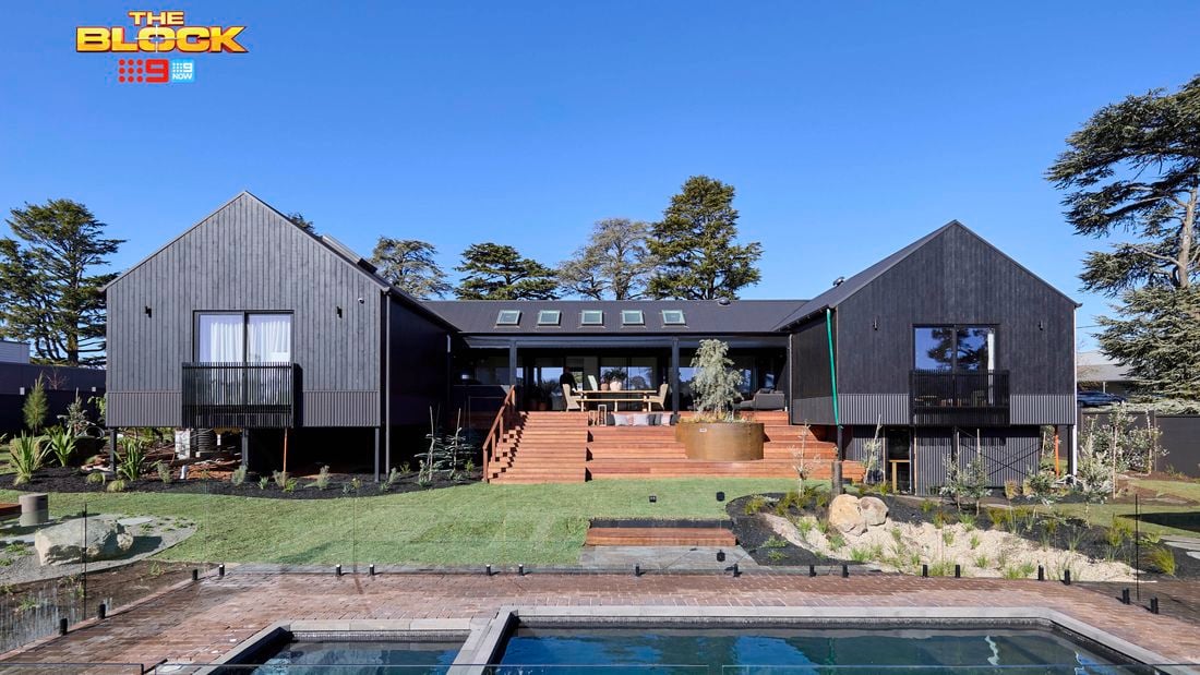 The back of a house with a pool in it, a rocked area, timber decking and many plants in it.
