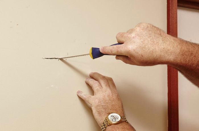 A person cutting into a plasterboard wall using a plaster saw