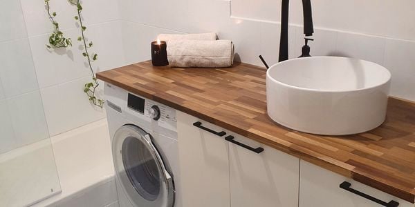 Bathroom with timber benchtop, round sink and black tapware next to a bath and shower