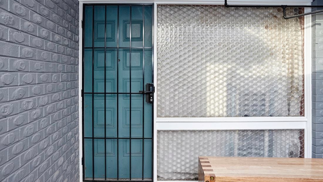 A barred security door fitted to the outside of a blue timber front door next to a circular patterned glass window