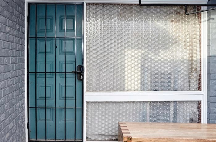A barred security door fitted to the outside of a blue timber front door next to a circular patterned glass window