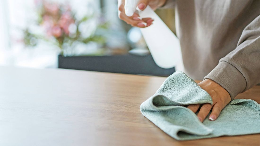 A person cleaning a wooden surface with a spray bottle and a cloth.
