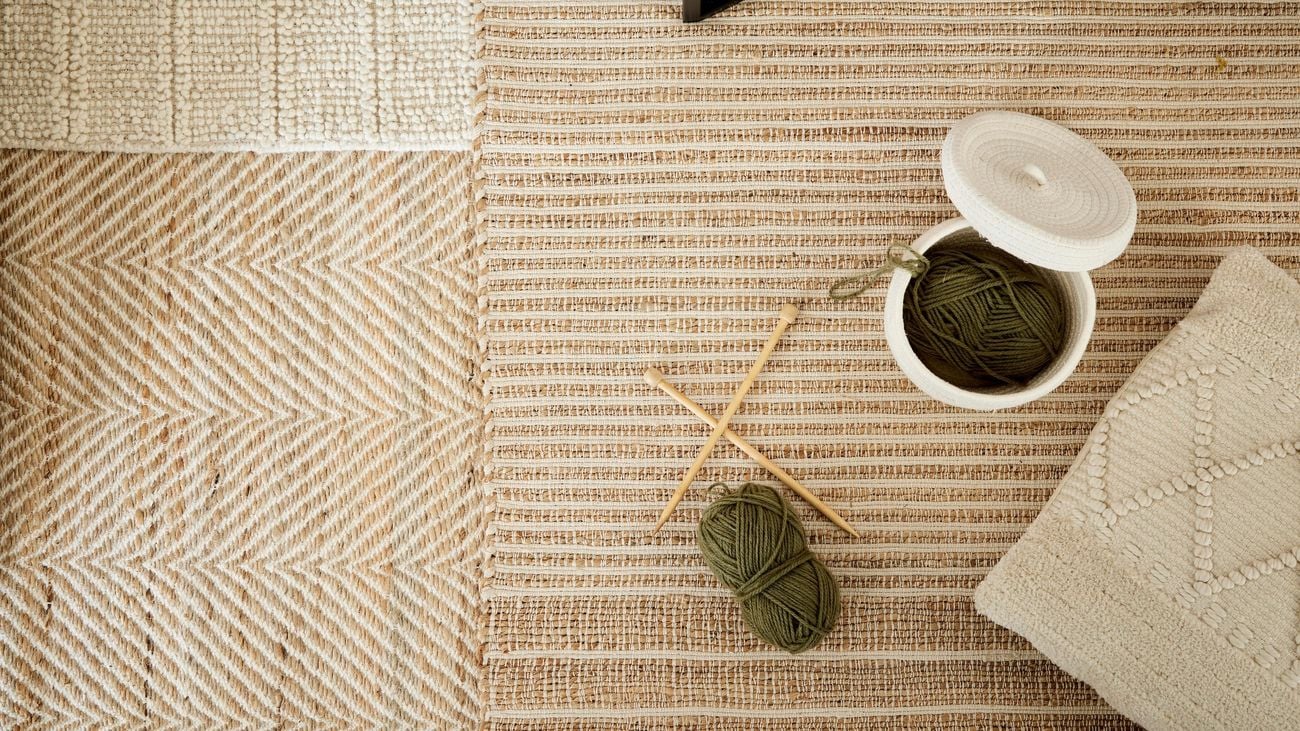 Bird’s-eye view shot of multiple beige rugs layered over the top of each other with knitting placed on top.