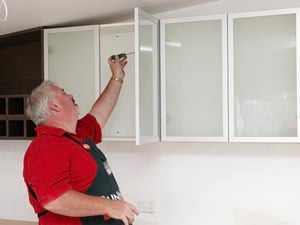 Person attaching a glass door to a kitchen wall cabinet