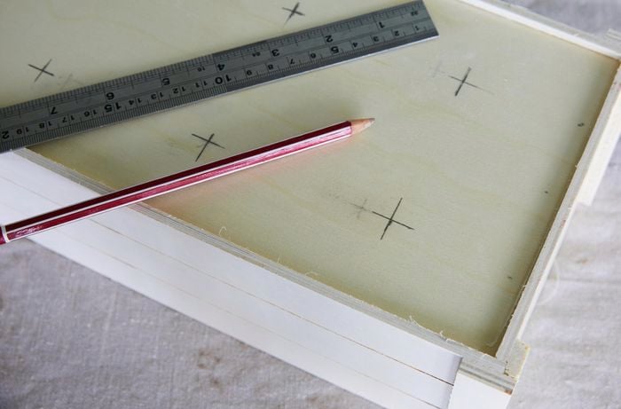 A wooden crate with crosses marked on the bottom in pencil. A pencil and a ruler lay on top of it