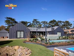 The back of a house with a pool in it, outdoor lounge, rocks area and an outdoor fireplace in it.