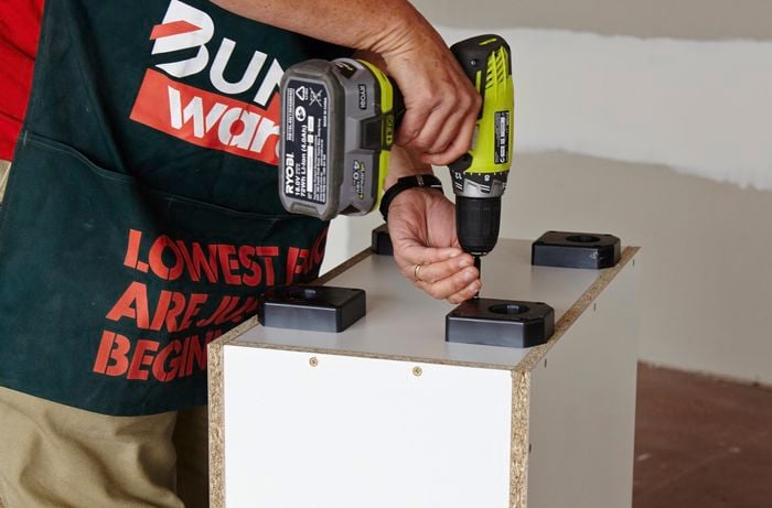 Person attaching plastic feet to cabinet using a drill
