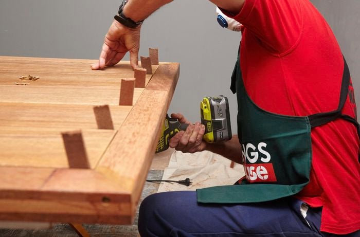 Person drilling into a wooden table that is upside down.