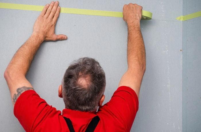 Man taping the area  of the wall to be waterproofed. 