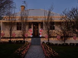 Cream traditional Australian style home with warm fairy lights across the roof, veranda and bushes along with light up candy canes as well as red and white decorative lollipops.