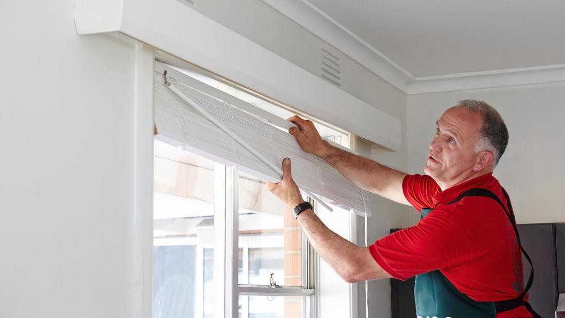 A person installing venetian blinds in a window