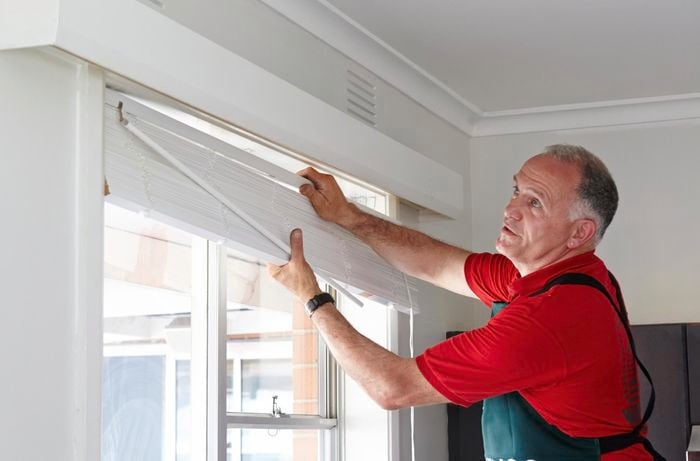 A person installing venetian blinds in a window