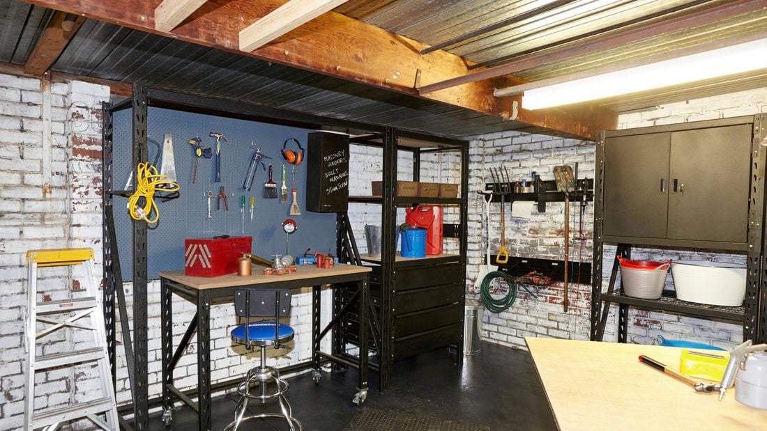 A garage with a pegboard and steel shelving units and cabinets and a retro stool