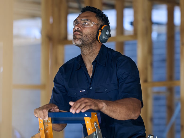 Justin O’Neil on a worksite on a Citeco ladder, wearing earmuffs and safety glasses