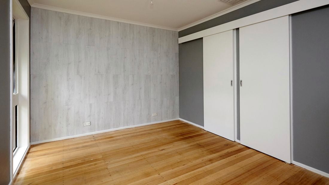 An empty room with a timber floor and a pale timber looking feature wall
