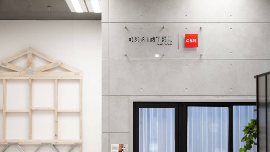 Building materials display featuring Cemintel wall cladding panels, window systems and timber framing construction samples in a showroom environment.