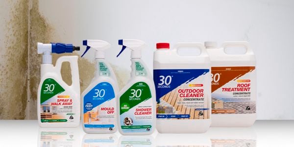 Five bottles of 30 second spray cleaner in front of a white wall with mildew on it.