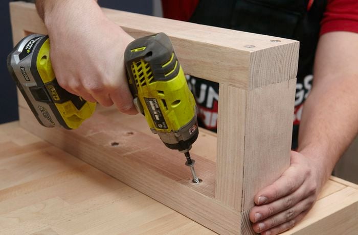 Person drilling arm rests of timber lounge to the base panel.