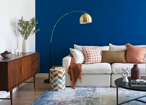 A living room with a navy blue wall, couch, buffet table and rug.