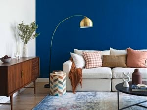 A living room with a navy blue wall, couch, buffet table and rug.