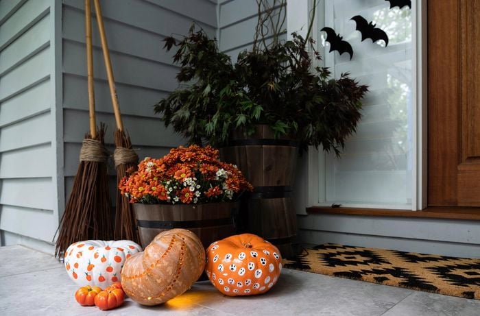 Decorated pumpkins styled at the outside entrance of a house with some broomsticks.