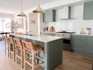 A modern kitchen with green cupboards, marble benchtop, with bar stools at the bench and timber flooring. 