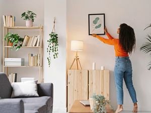 A woman hanging a print on a wall in a living room.