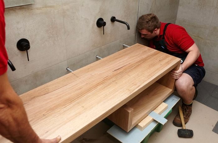 Two people sliding a vanity unit onto reo bars extending from holes in a bathroom wall