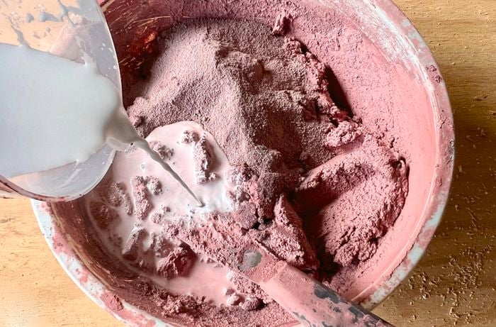 A person pours a bonding agent into a pink cement mix.