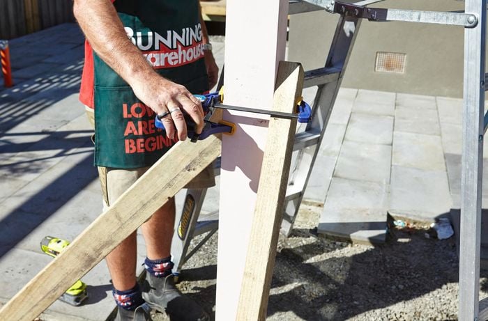 Bunnings team member positioning a length of wood against a standing post using a clamp