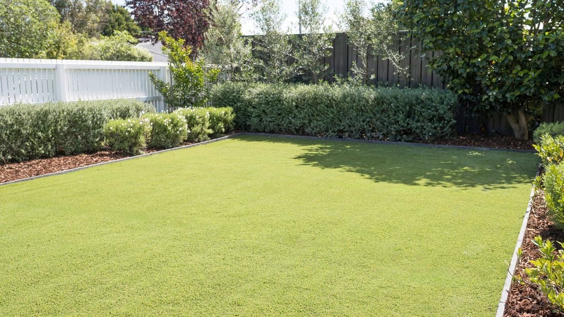 Neatly installed synthetic turf lawn is surrounded by well-maintained garden beds and greener