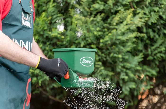 A person using a fertiliser spreader to spread weed killer on a lawn