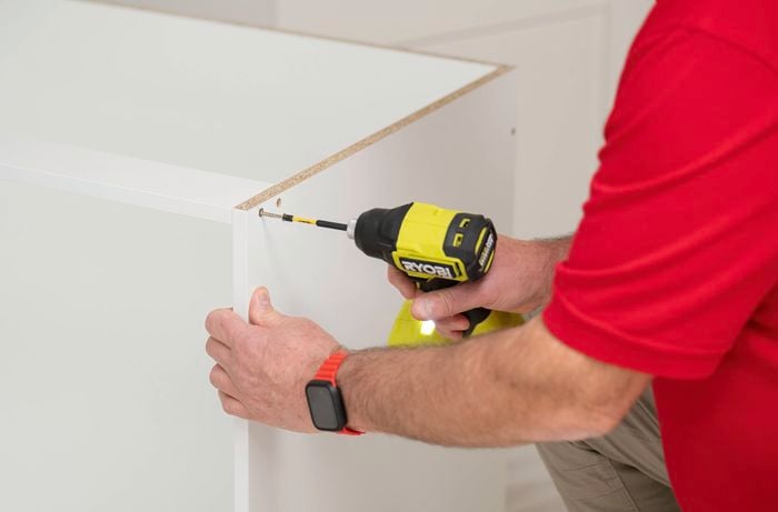 A person is using a power drill to attach a support rail that helps keep the cabinet strong and hold its shape over time