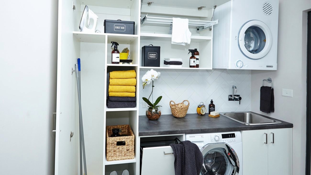 Tidy broom cupboard featuring brooms, towels, a washing machine and dryer.
